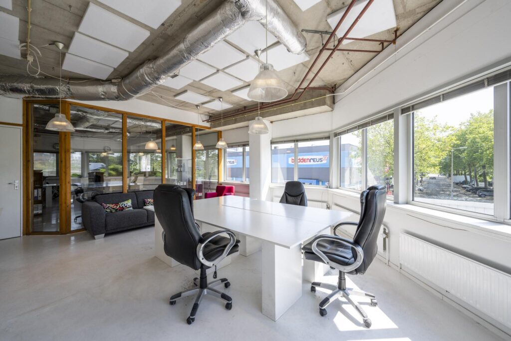 Licht en modern kantoor aan de Anthony Fokkerweg met vergadertafel, bureaustoelen en grote ramen met uitzicht op de straat.